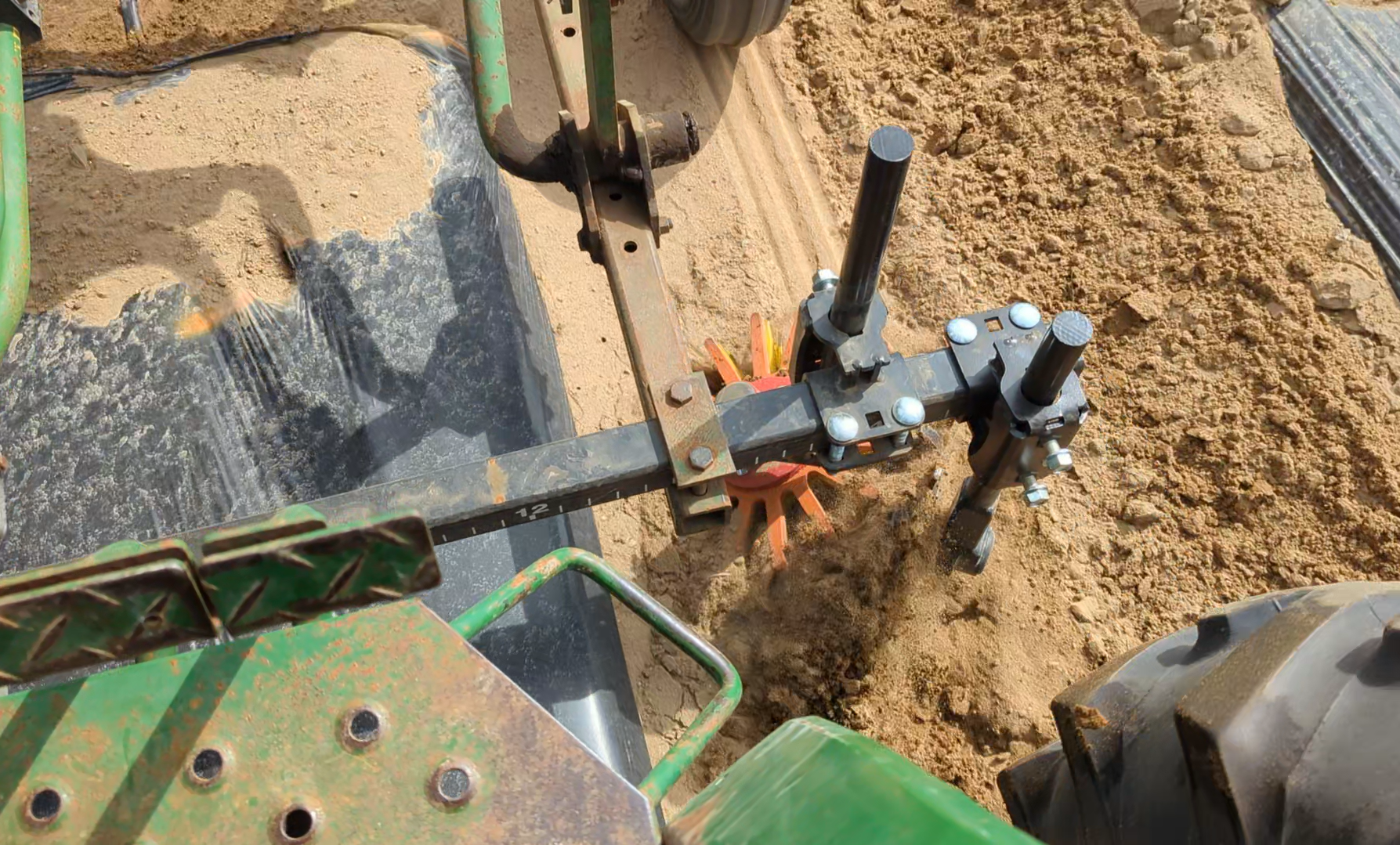 A finger weeder fracturing sandy soil near the edge of a plastic row cover.